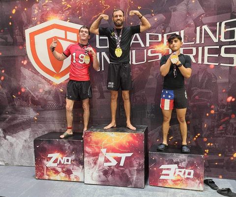 Adult Venice BJJ competitor flexing on top of a No-Gi tournament podium with a gold medal